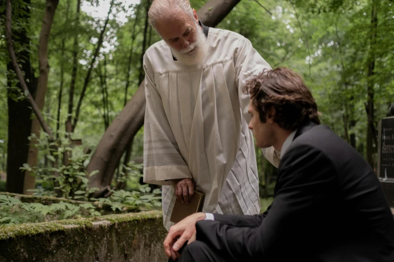 the priest stands on stone platform in the forest with another person near by