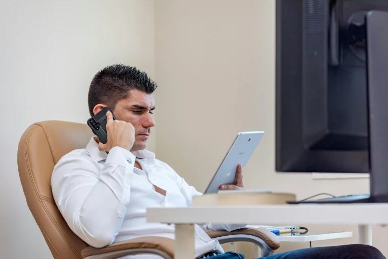 a man is sitting down and talking on the phone with his lap top