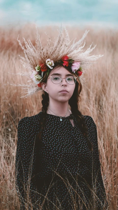 woman with flowers on her hair, wearing glasses and standing in tall grass