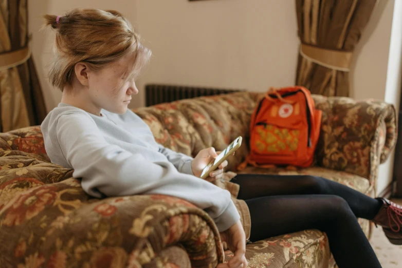 girl sitting on couch looking at cell phone with bag nearby