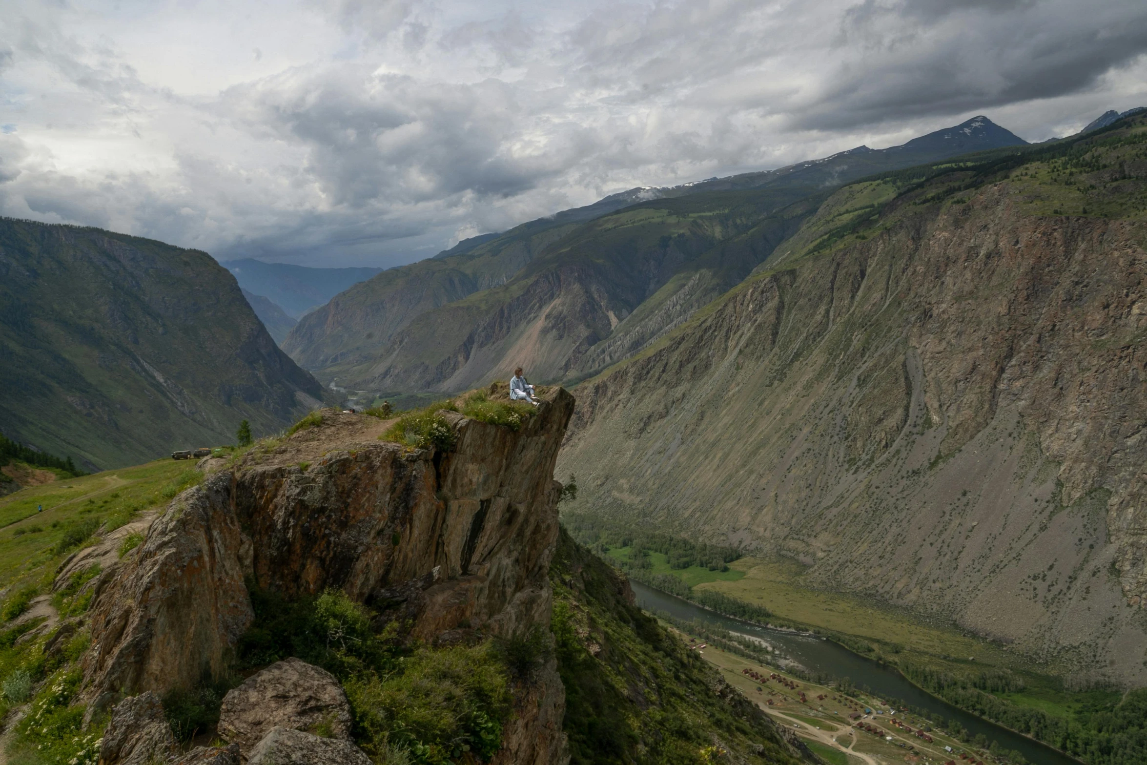 a person sitting on a cliff near mountains