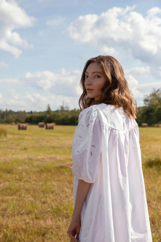 a woman stands in an open field with animals in the distance