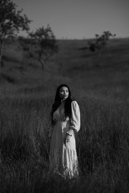 a woman stands in a field in front of trees