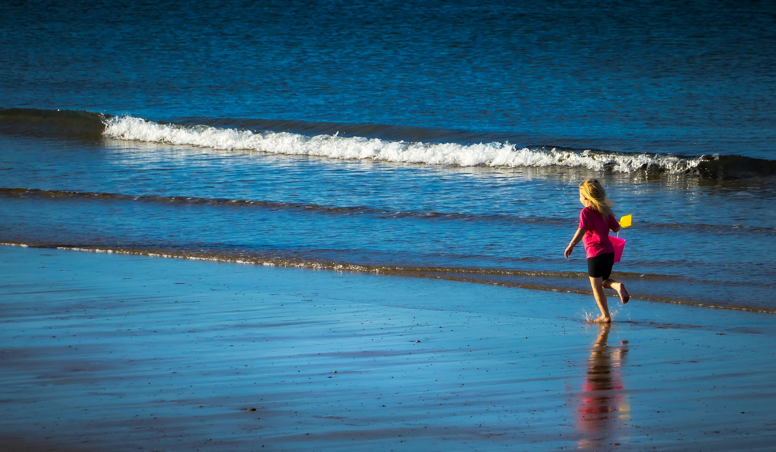 a little girl running on the beach towards the water