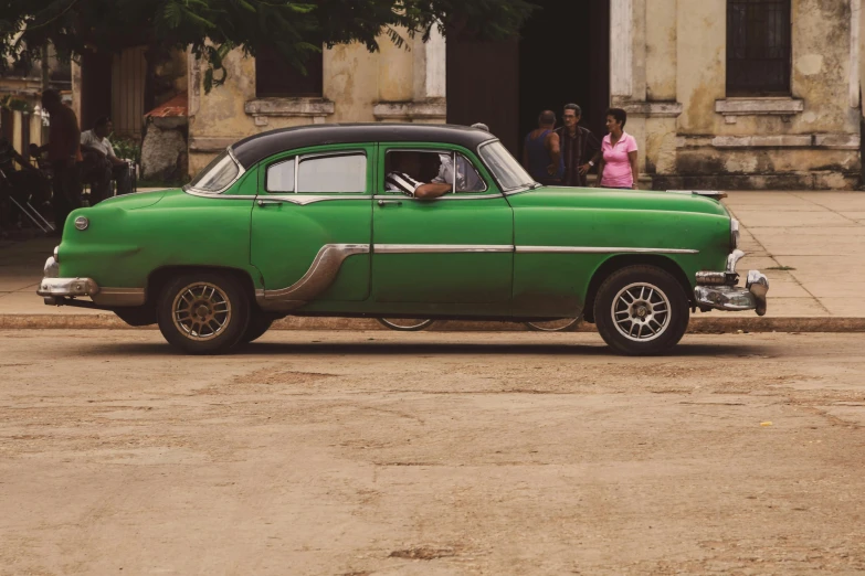 a green old car parked on the side of a road