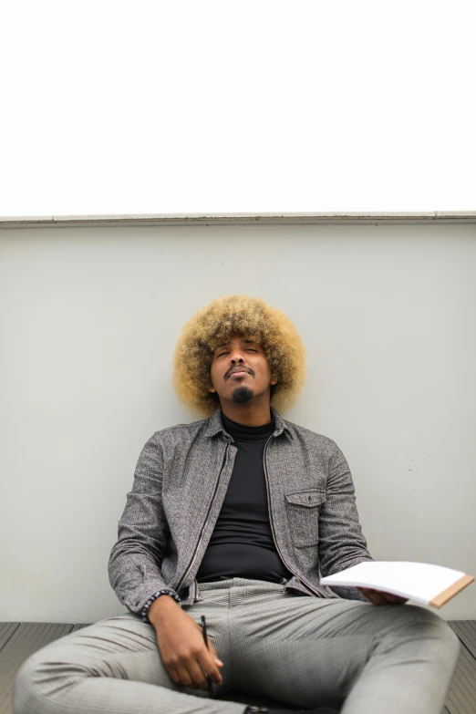 a man with long hair sits in front of a wall