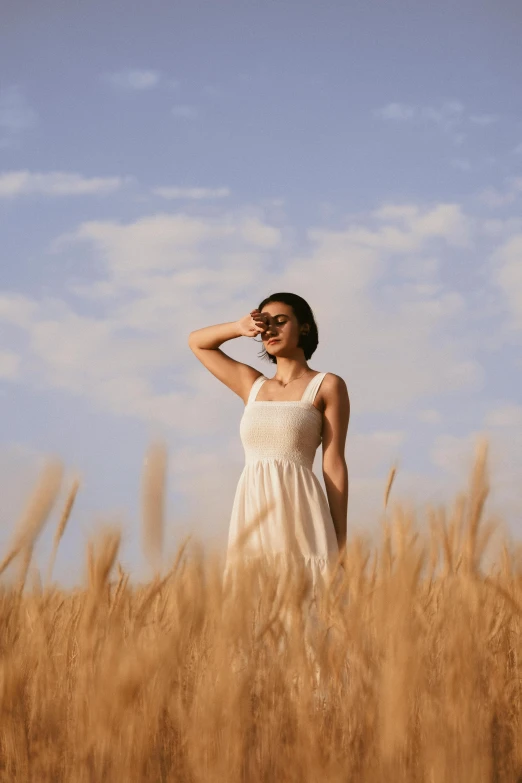 a woman in a white dress standing in some grass with her hands on her hips