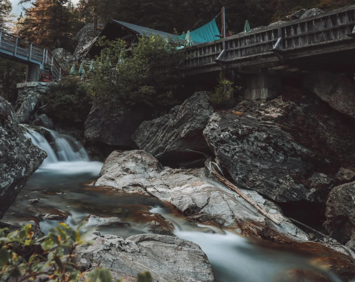 a waterfall running under a bridge near a forest