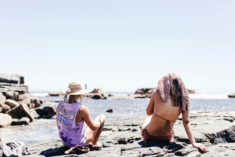 two women sitting on a beach next to the ocean