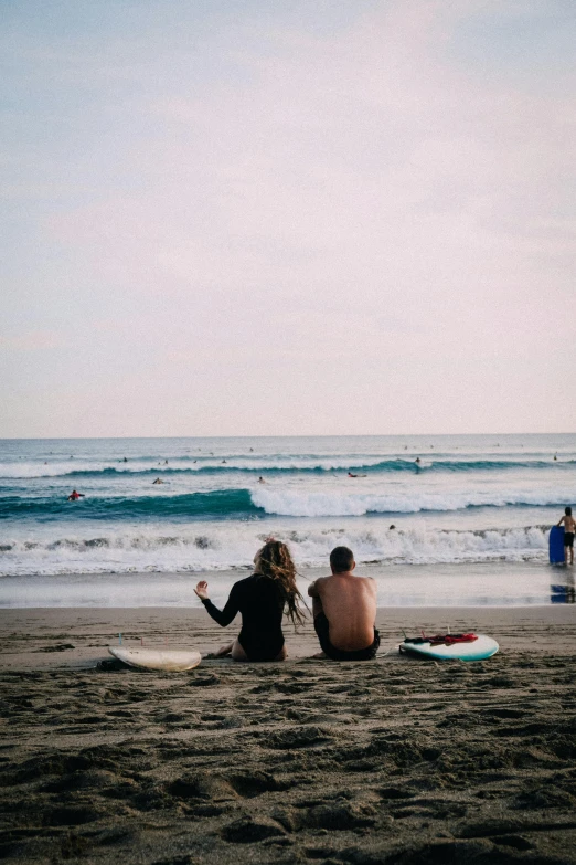 two people sit on a beach while the tide rolls in