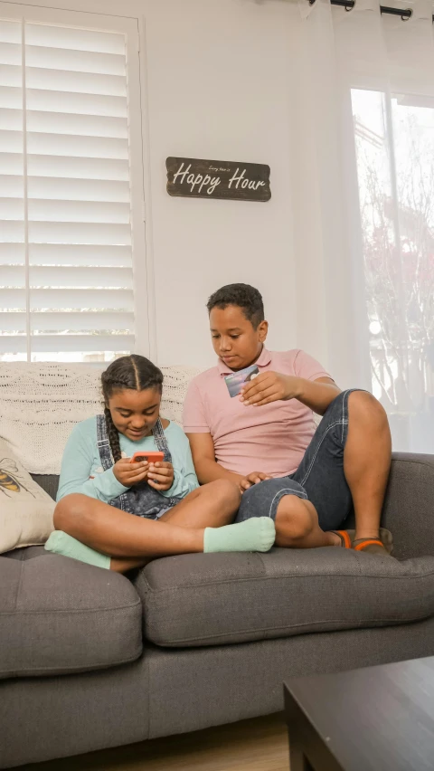 two children sitting on a couch and looking at their phones