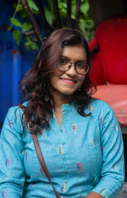 a smiling woman wearing glasses standing next to a wall