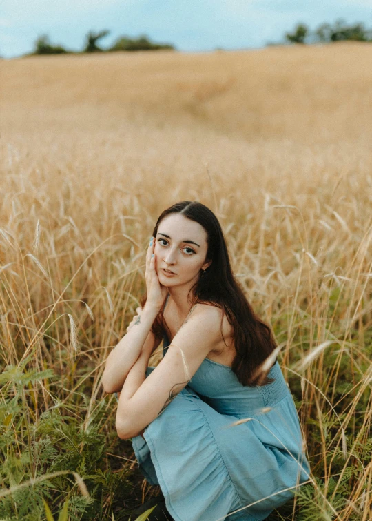 a young woman sitting on the grass in front of a field