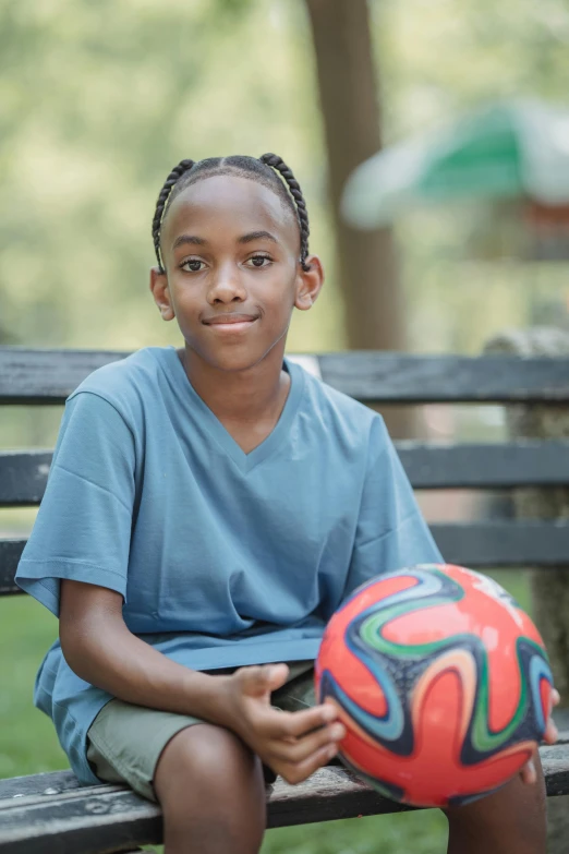 a boy that is sitting on a bench holding a soccer ball