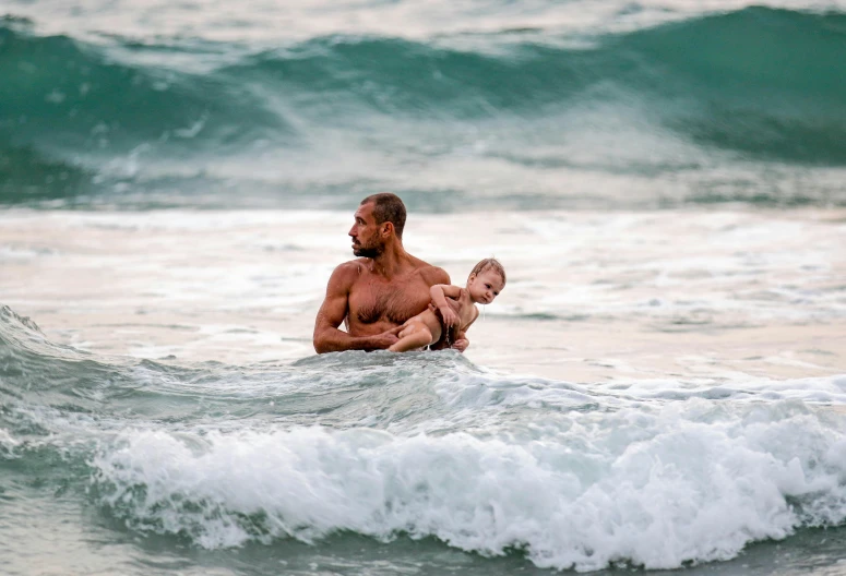 a man holding a baby riding on top of a wave