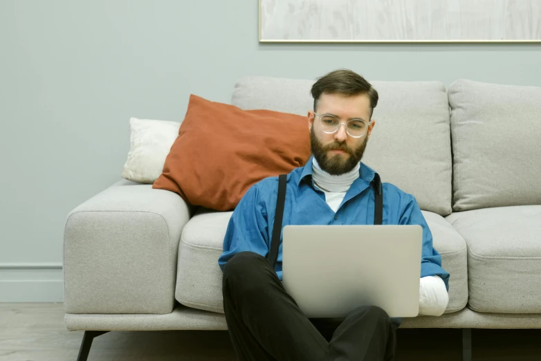 man in blue shirt sitting on couch using laptop