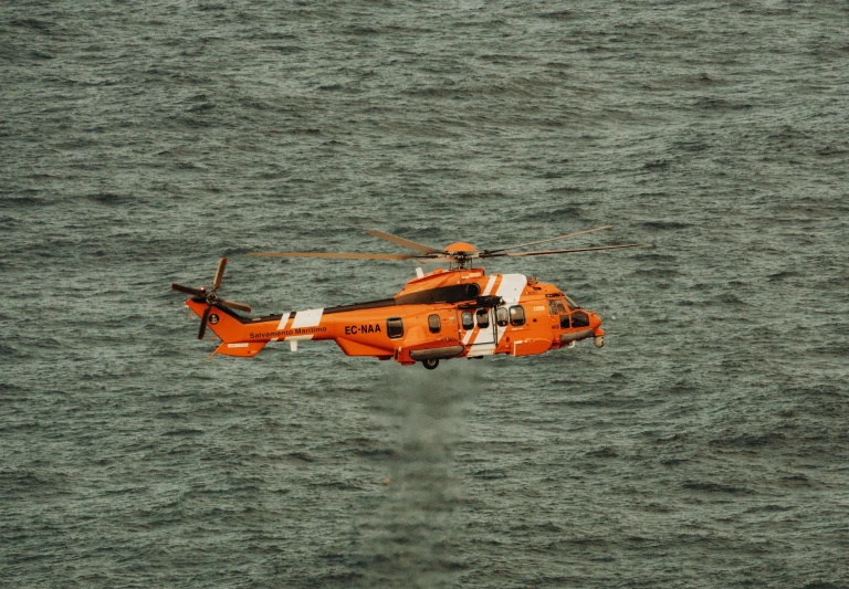 an orange helicopter flying over the ocean water