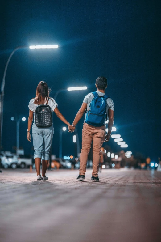 two people holding hands while walking across the street at night