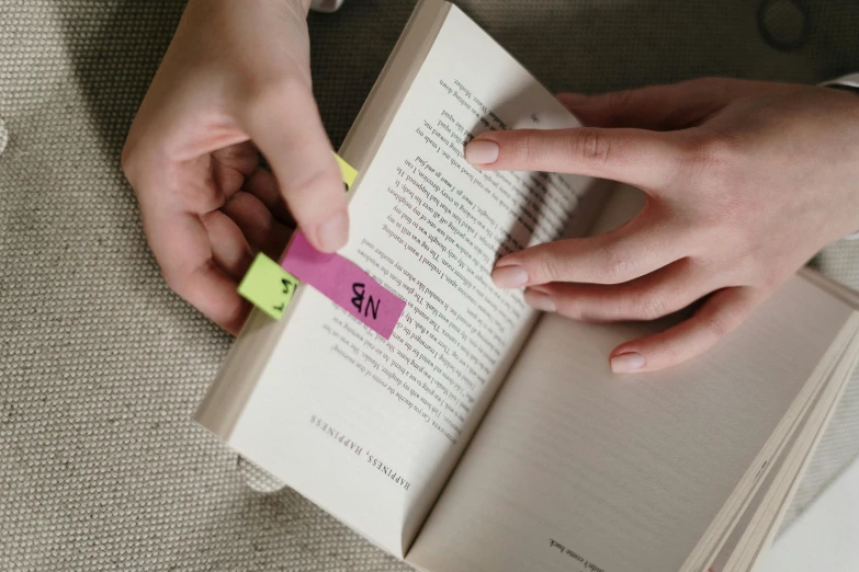 the person is holding a sticky note and reading a book