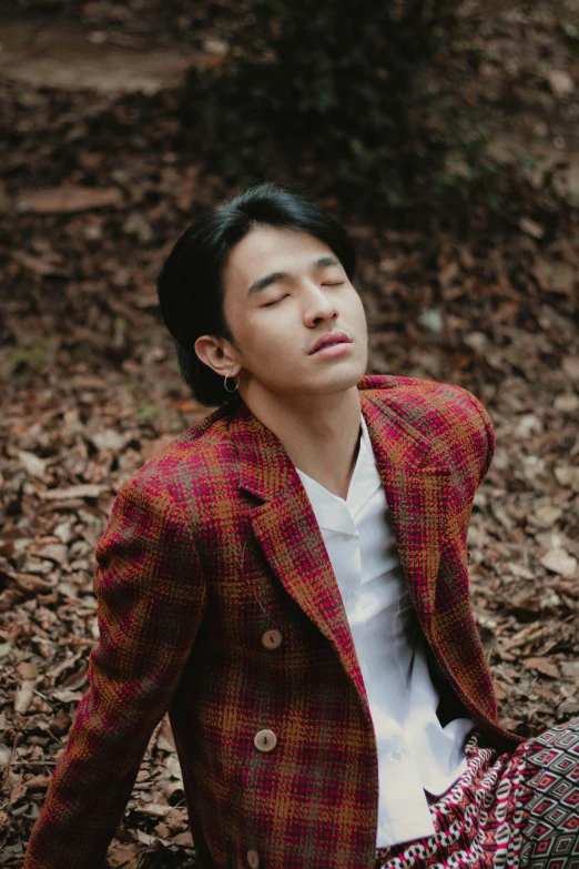 a young man sitting in the woods wearing a jacket