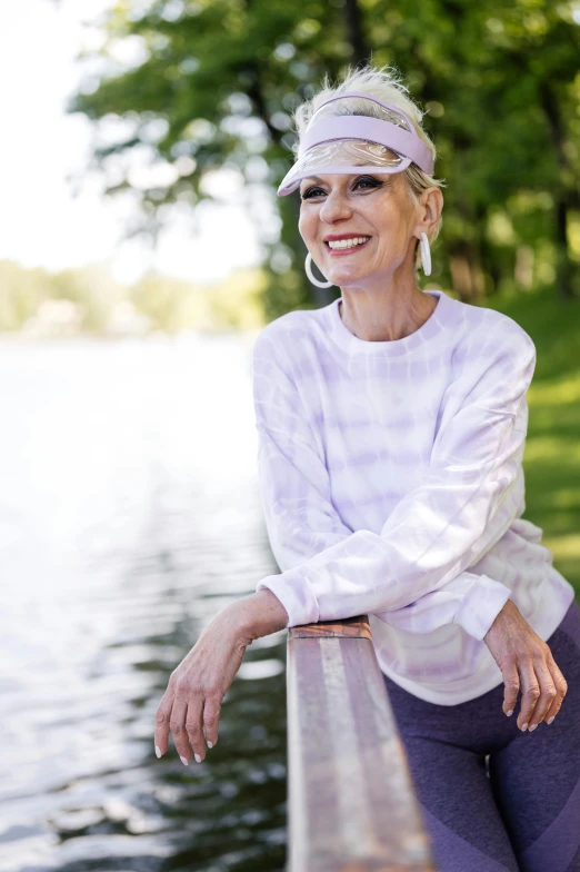 a woman poses next to a river and a bench