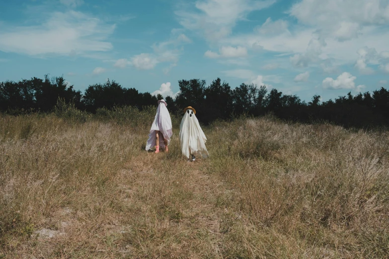 two women wearing white clothes are walking through a field