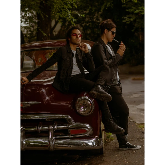 two people are sitting on the hood of an old fashioned car