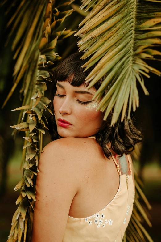 a beautiful young woman standing under a palm tree