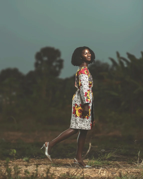 a woman in a patterned shirt dress poses by the woods