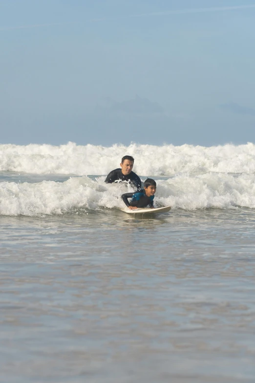 two people in wet suits surfing on a white surfboard