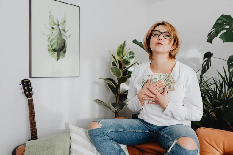 a woman wearing glasses sits on a couch and holds onto her money