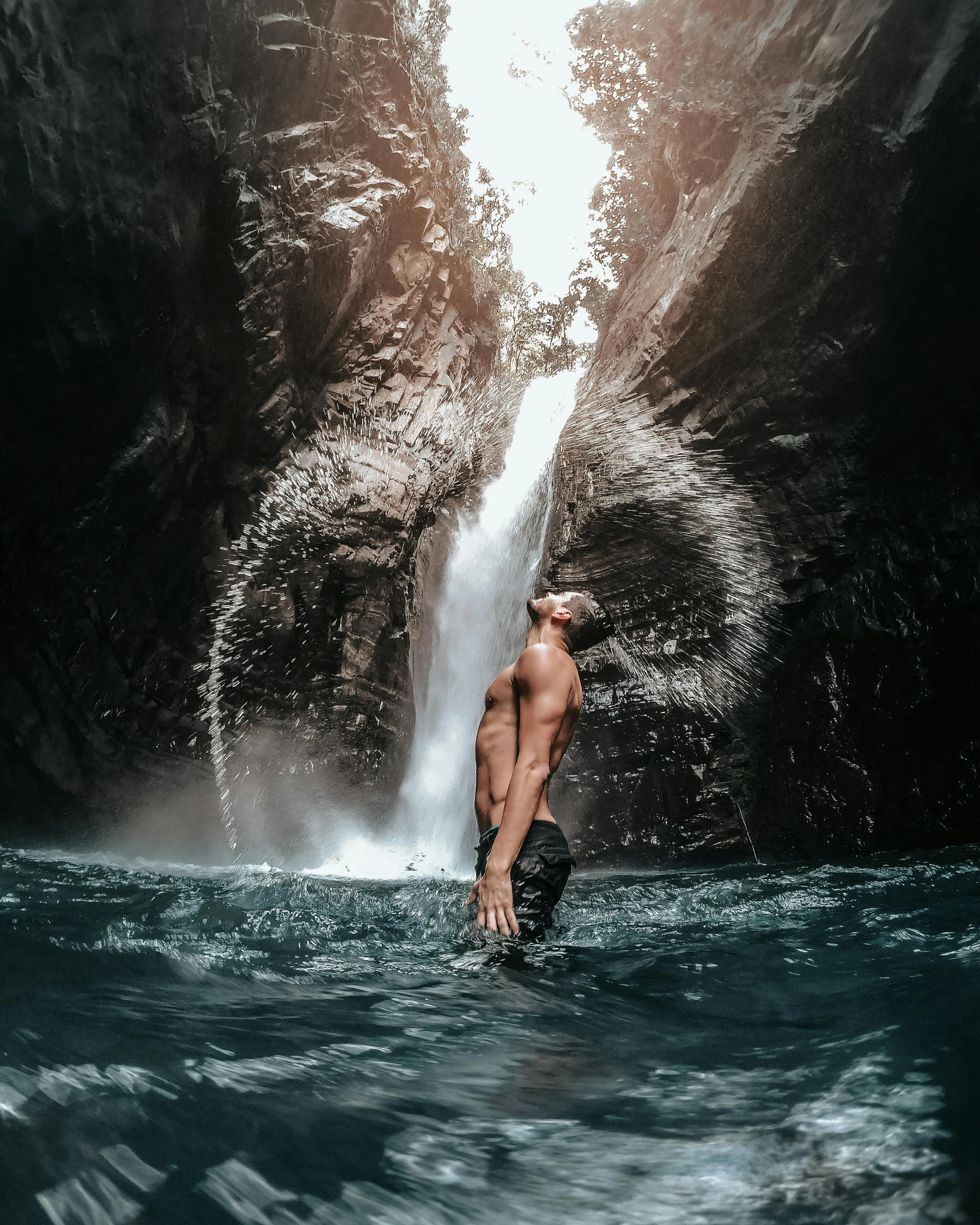 a man standing in a body of water with waterfall behind him