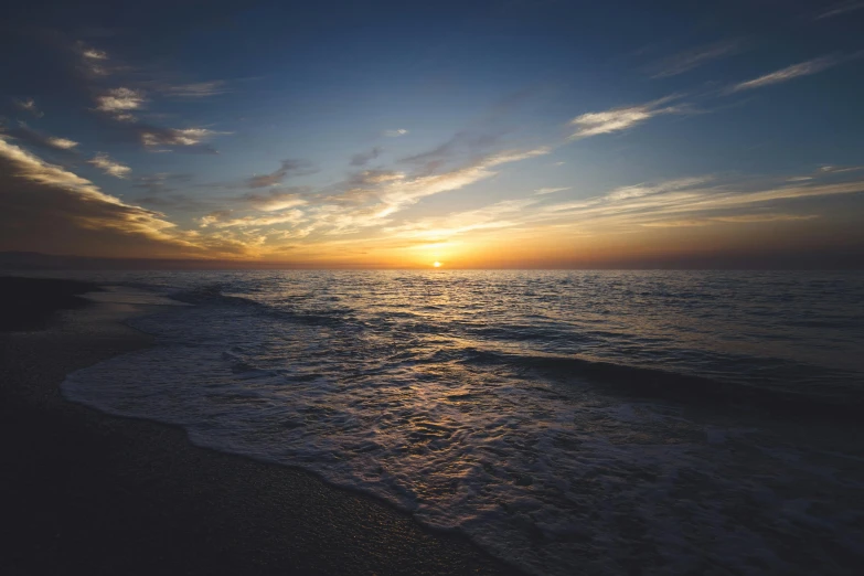 the sun is setting over the water near the beach