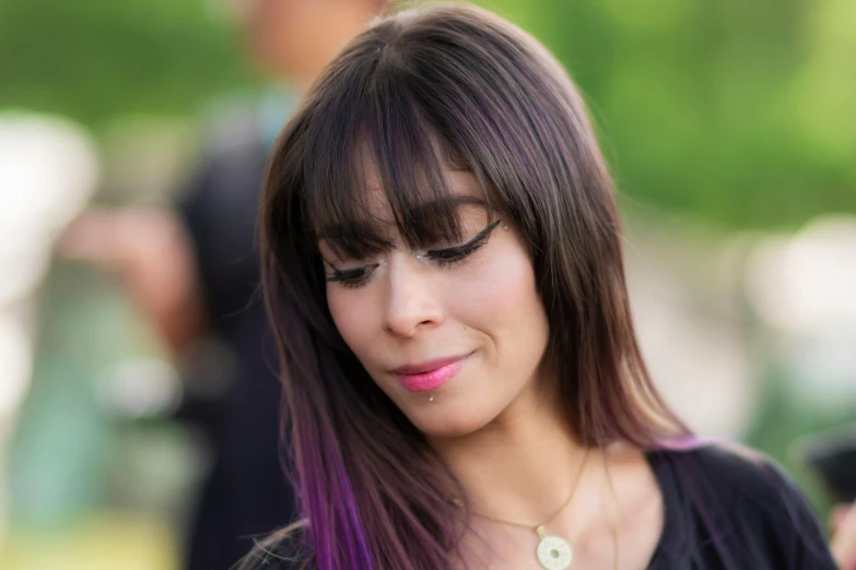 a young woman wearing a necklace and looking down while she uses her cell phone