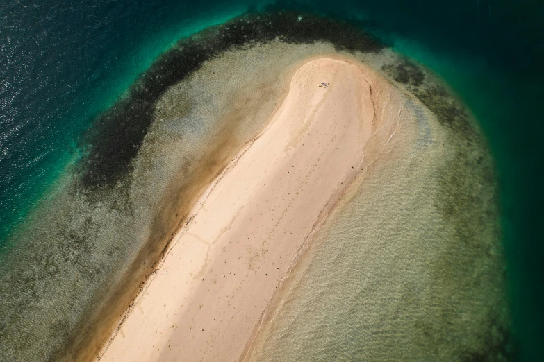 an aerial po shows the sandy island, which has a blue green water and white sand