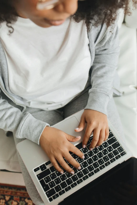 a girl is sitting on a bed typing on a laptop