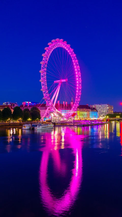 large wheel displayed at night overlooking waterway with lit - up boats