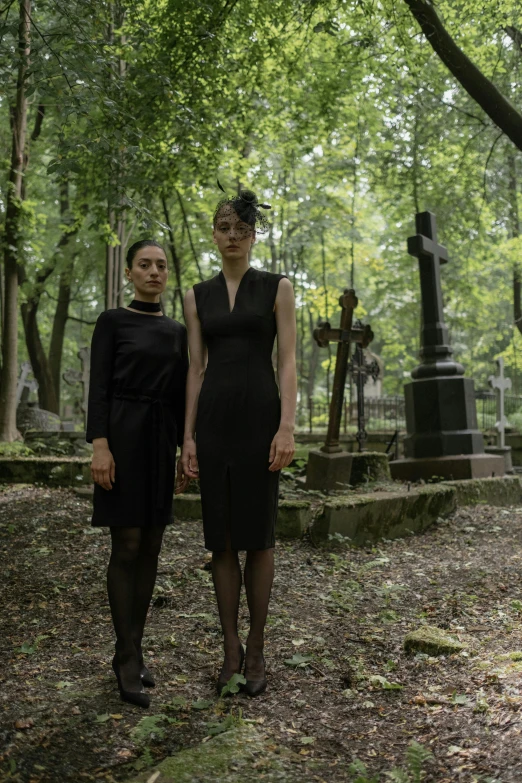 two women in black dresses walking through a forest