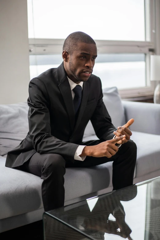 a man in a suit sits on a couch while holding a cigar