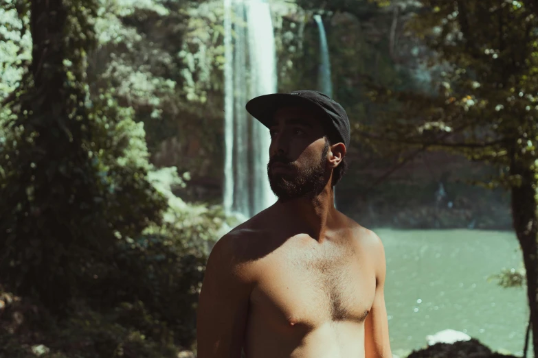 a man standing by a waterfall, with a hat on his head