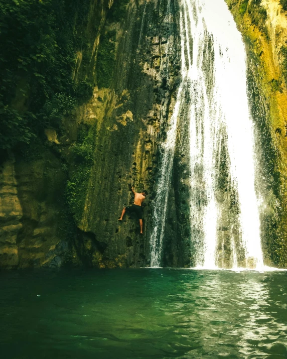 a man jumping off a waterfall into a body of water