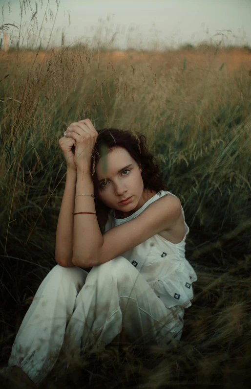 a girl sitting in tall grass posing for a pograph