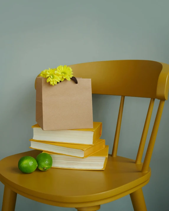 a wooden chair with two books, two limes and one brown bag with yellow flowers on it