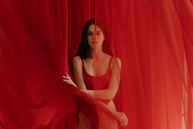 a woman is sitting on a curtain while wearing a red 