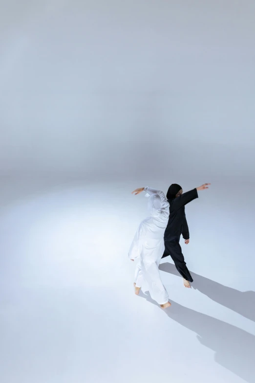 two people with white clothing dance in a light room