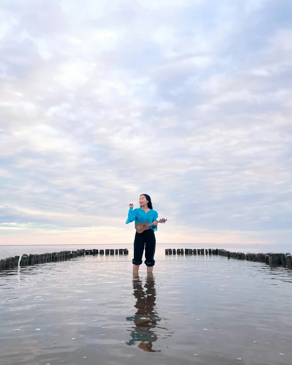 a woman standing in the water with a blue kite