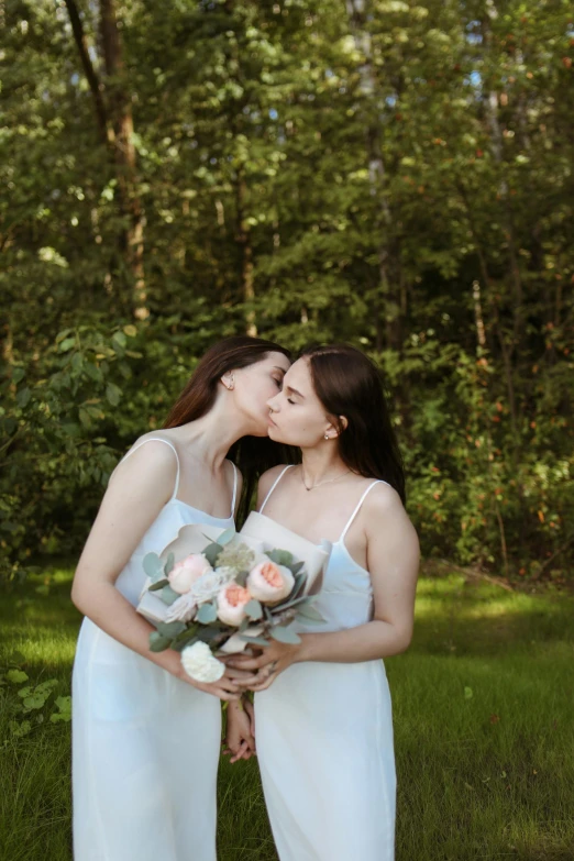 two women in white dresses one is kissing and the other is holding flowers