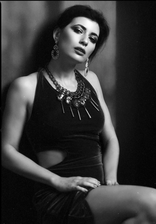 a woman wearing some necklaces sitting in front of a wall