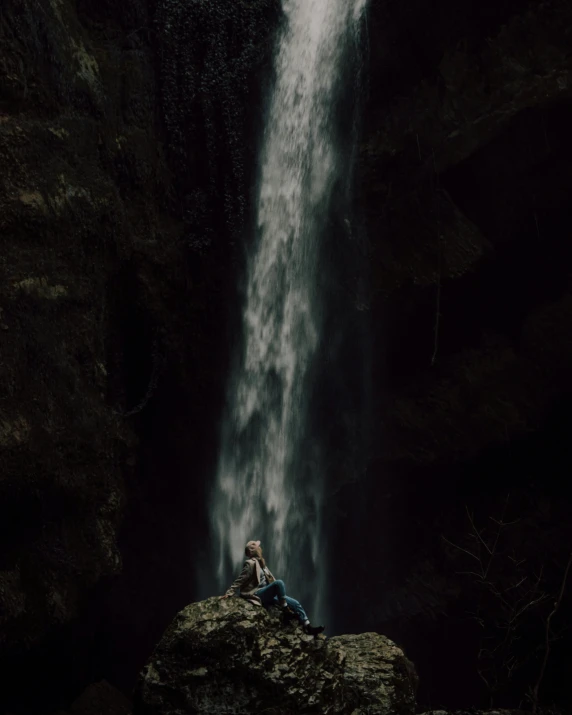 a woman sitting on top of a rock in front of a waterfall
