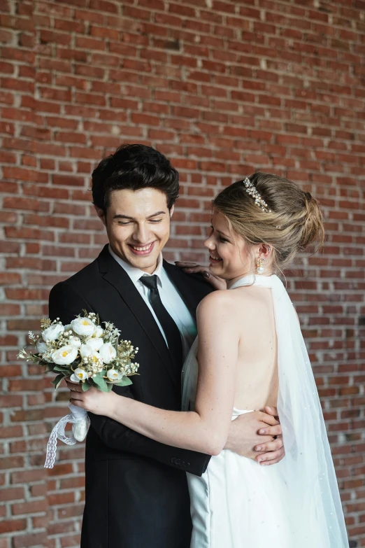 a bride and groom hugging and posing in front of a brick wall